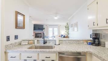 A kitchen with granite countertops, a stainless steel sink, white cabinetry, a built-in oven, and a ceiling fan.