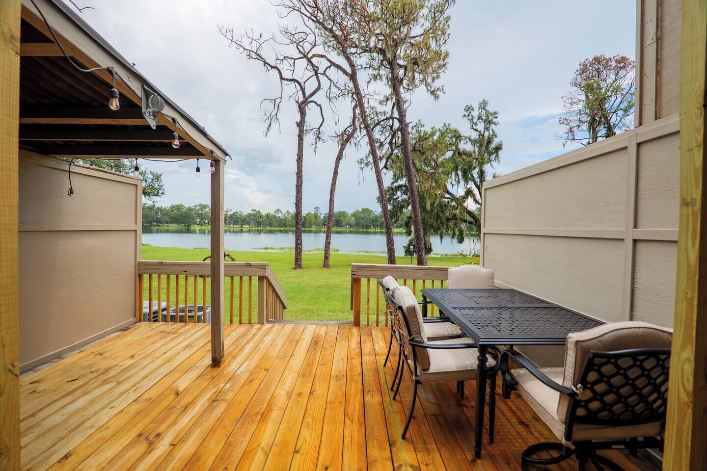 A wooden deck with a table and chairs, overlooking a lake with trees.