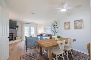A dining area with a wooden table and chairs, a ceiling fan, and a fireplace.