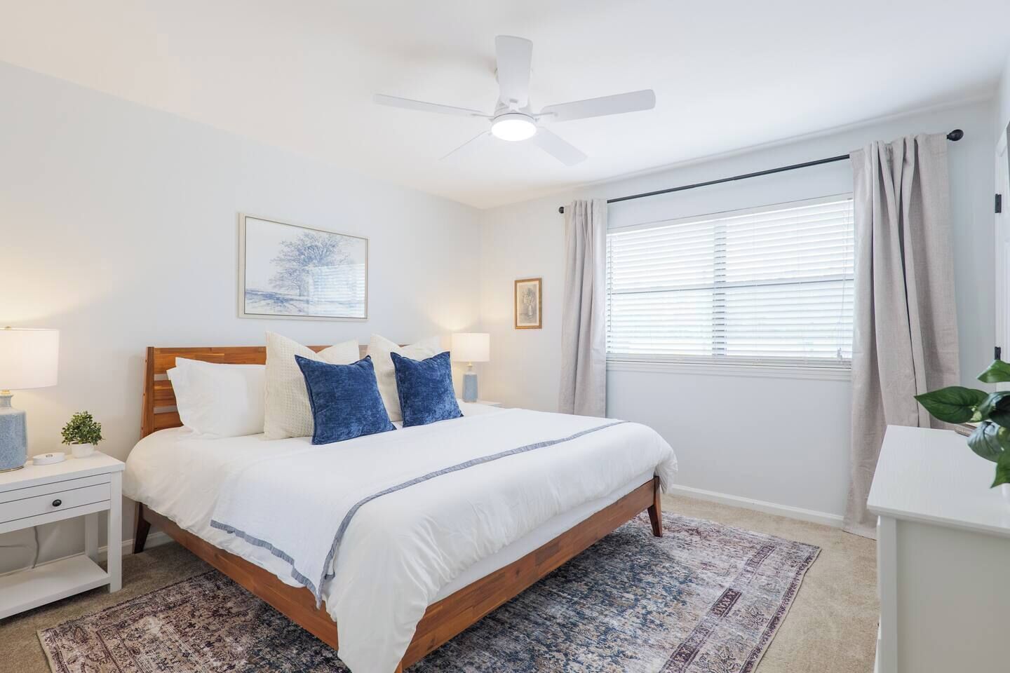 A bedroom with a bed, nightstands, a ceiling fan, a window with curtains, and a rug.