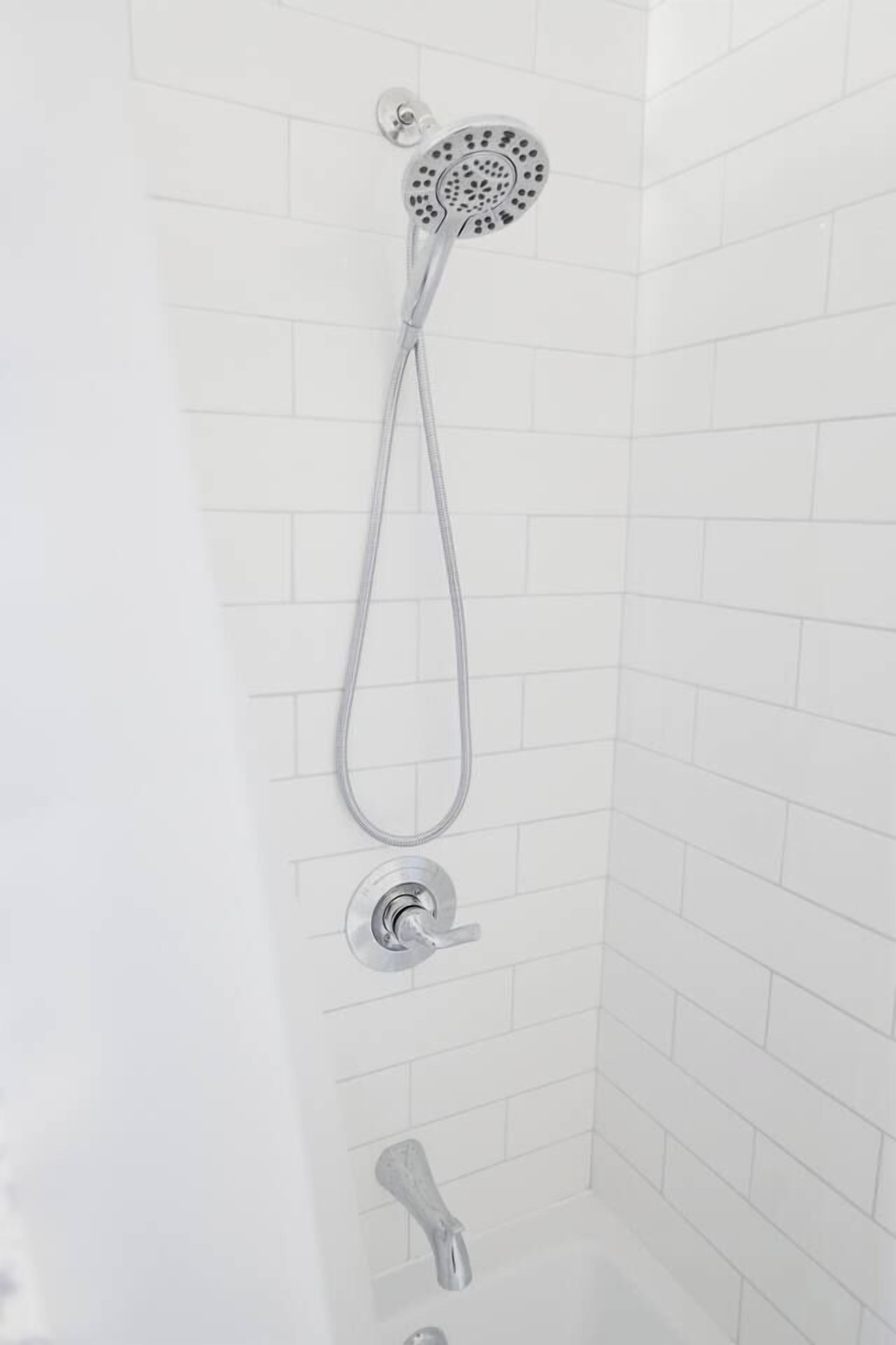 Ducha con cabezal de ducha de mano y grifo empotrado en un baño con azulejos.