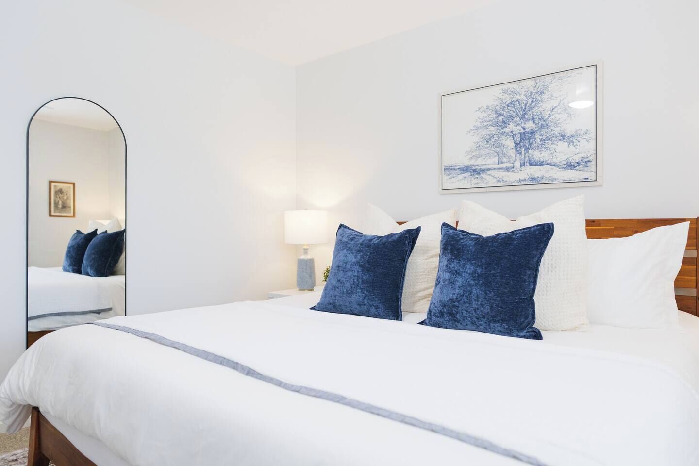 A hotel room with a large bed, a bedside lamp, a framed picture on the wall, and a mirror.