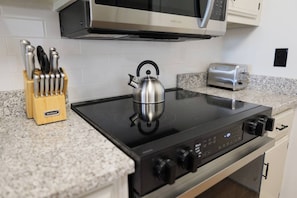 Eine Küche mit einem schwarzen Induktionskochfeld, einem Edelstahl-Wasserkocher, einem Toaster und einem Messerblock.