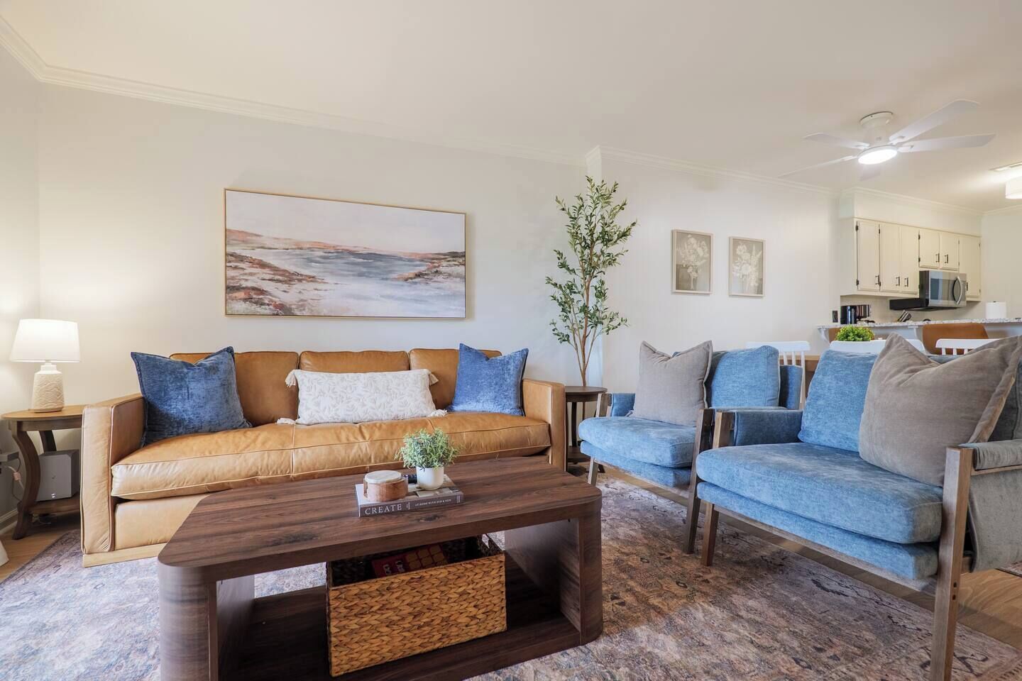 A living room with a brown sofa, blue armchairs, a wooden coffee table, and a painting on the wall.