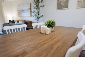Ein Esstisch mit Holzplatte, umgeben von weißen Stühlen und einem kleinen Blumentopf mit Grünpflanzen.