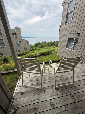 A wooden deck with two metal chairs overlooking a landscaped garden and a body of water. - 3 Bedroom Condo with stunning sunset views located in The Homestead Resort! (Glen Arbor)
