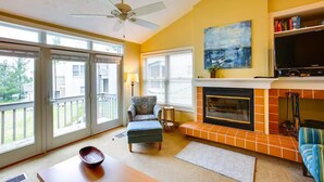 A living room with a fireplace, a ceiling fan, and a large window. - 3 Bedroom Condo with stunning sunset views located in The Homestead Resort! (Glen Arbor)
