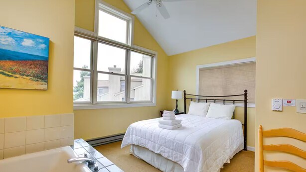 A bedroom with a bed, a window, a ceiling fan, a bathtub, and a painting on the wall. - 3 Bedroom Condo with stunning sunset views located in The Homestead Resort! (Glen Arbor)