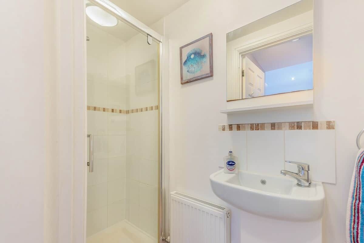 Ein Badezimmer mit Duschkabine aus Glas, einem weißen Waschbecken mit Spiegel darüber und einem Handtuchhalter rechts.