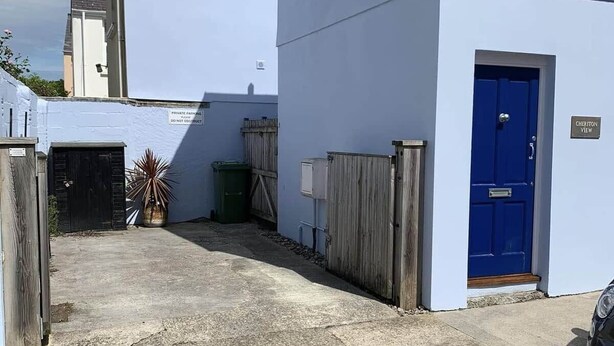 A building with a blue door, a white exterior, and a concrete driveway. - Cheriton Ground Floor includes EV Charge Parking & Dog (Tenby)