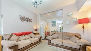 A living room with two sofas, a chandelier, and a kitchen in the background. - Cheriton Ground Floor includes EV Charge Parking & Dog (Tenby)
