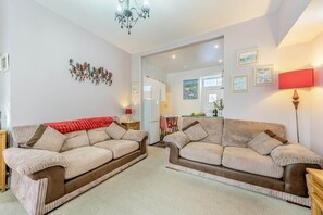 Ein Wohnzimmer mit zwei Sofas, einer Chandelieber und einer Küche im Hintergrund.