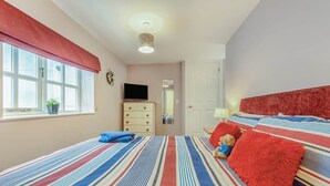 A bedroom with a striped bedspread, a television on a dresser, and a red headboard. - Cheriton Ground Floor includes EV Charge Parking & Dog (Tenby)