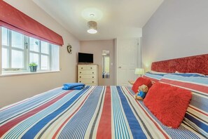 Ein Schlafzimmer mit gestreifter Bettdecke, einem Fernseher auf einer Kommode und einem roten Kopfteil.
