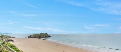 A beach with a clear sky, a sandy shore, and a rocky outcrop in the distance.
