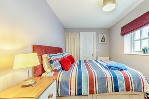 Ein Schlafzimmer mit Bett, Nachttisch mit Lampe, Fenster mit Vorhängen und einer Tür.