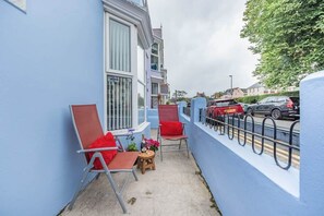 Ein Balkon mit zwei Stühlen und einem kleinen Tisch, Blick auf eine Straße mit parkenden Autos.