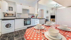 A compact kitchen with a washing machine, oven, and dining area set with a red polka dot tablecloth. - Cheriton Ground Floor includes EV Charge Parking & Dog (Tenby)