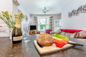 Ein Wohnzimmer mit Esstisch, gedecktem Tisch für eine Mahlzeit, einer Weinflasche und einem Brot.