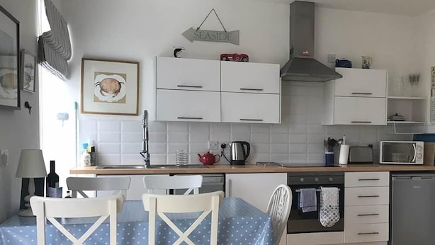 Keittiössä on valkoiset kaapit, mikroaaltouuni, vedenkeitin sekä ruokapöytä tuoleineen.