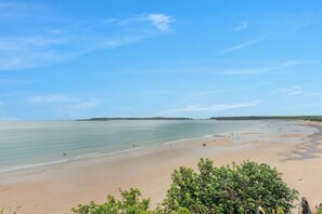 Ein Strand mit blauem Himmel und ruhigem Wasser, umgeben von viel Grün.