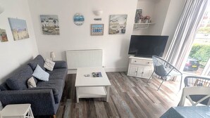 Olohuone, jossa on sohva, sohvapöytä, televisio ja taideteoksia seinillä.