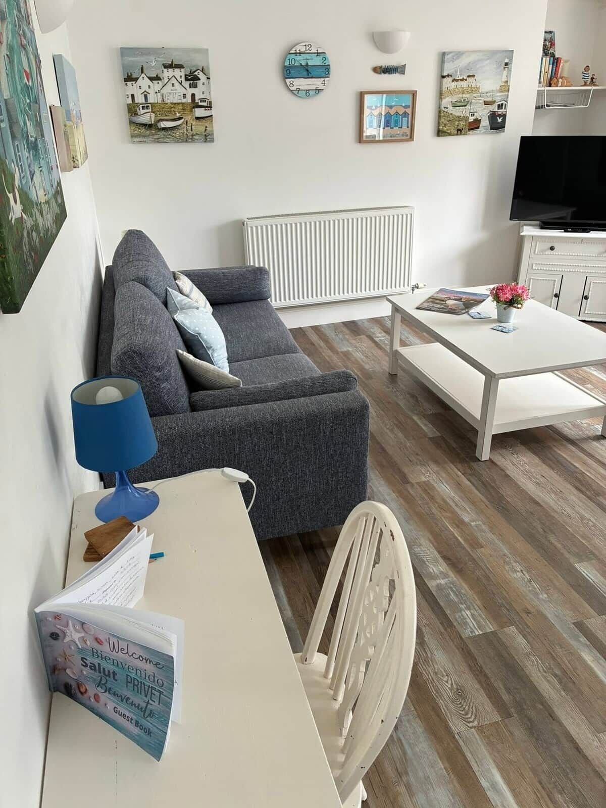Un salon avec un canapé gris, une table basse blanche, un meuble TV blanc et un radiateur blanc.