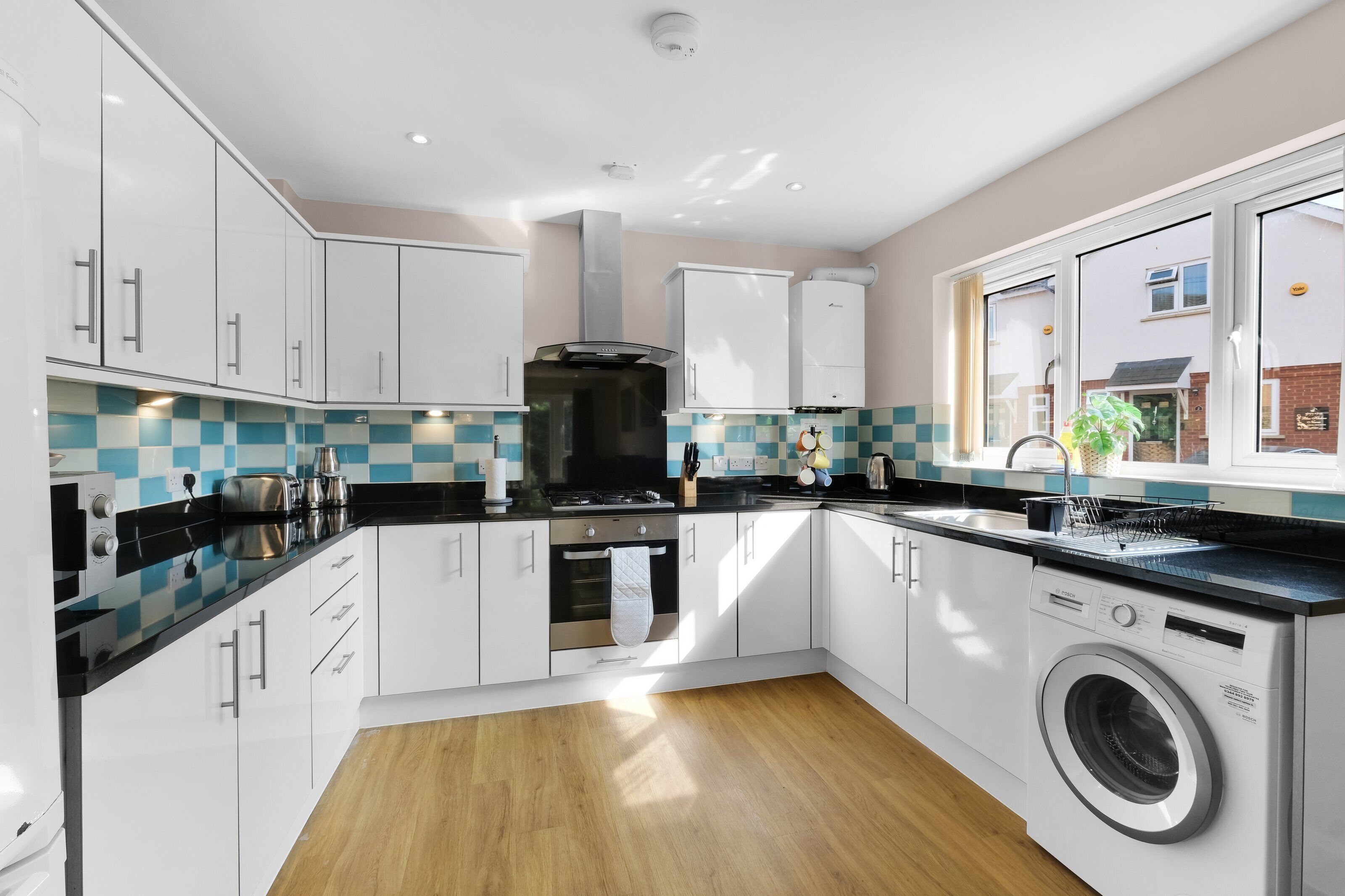 A modern kitchen with white cabinets, a black stove, and a Bosch washing machine.