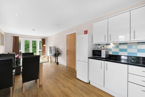 A modern kitchen with white cabinets, a black countertop, and a built-in microwave. - Heathrow Living 2BDR 2BA Apt 10-360stays (Stanwell)