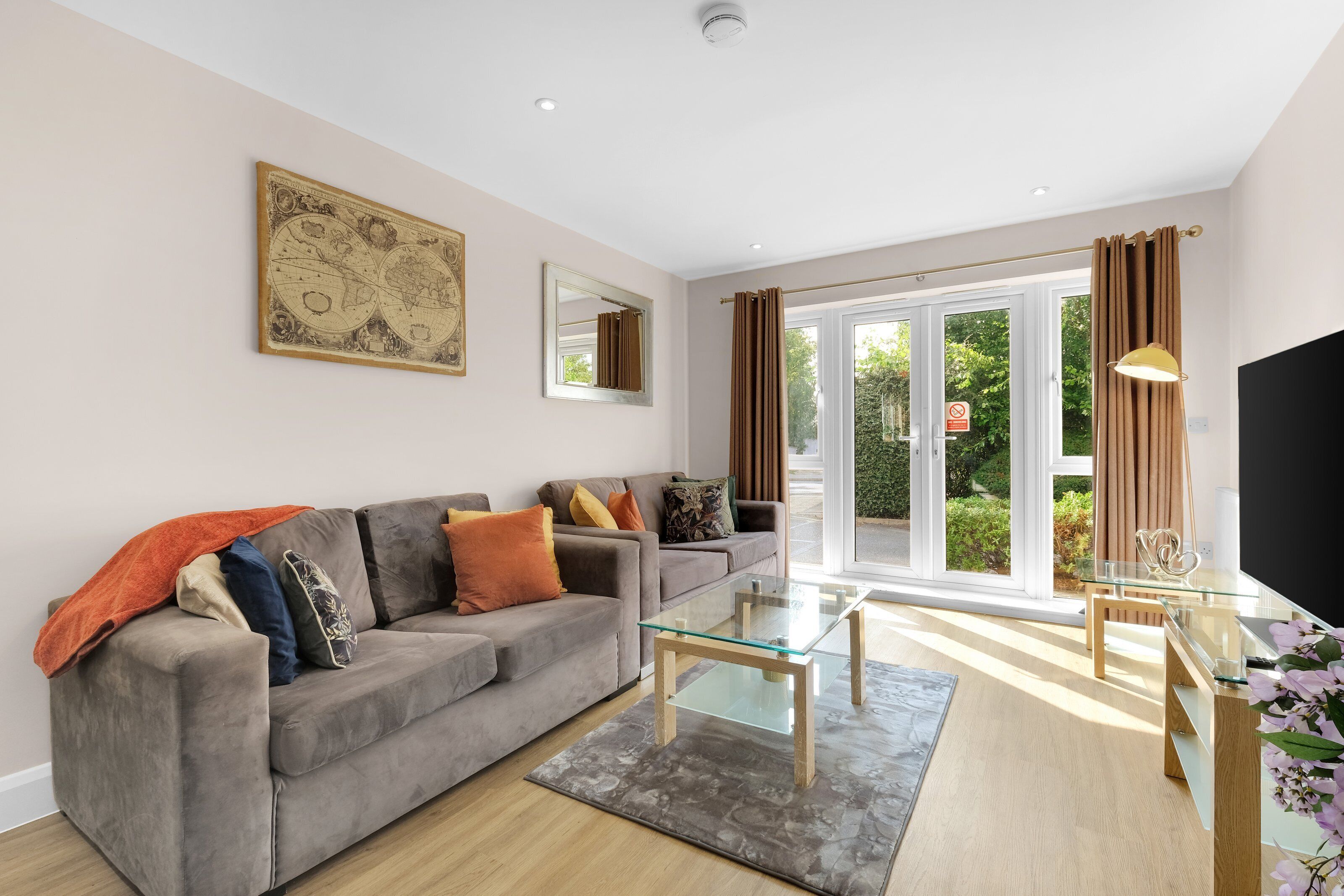 A modern living room with a grey sofa, a glass coffee table, and a large window with curtains.