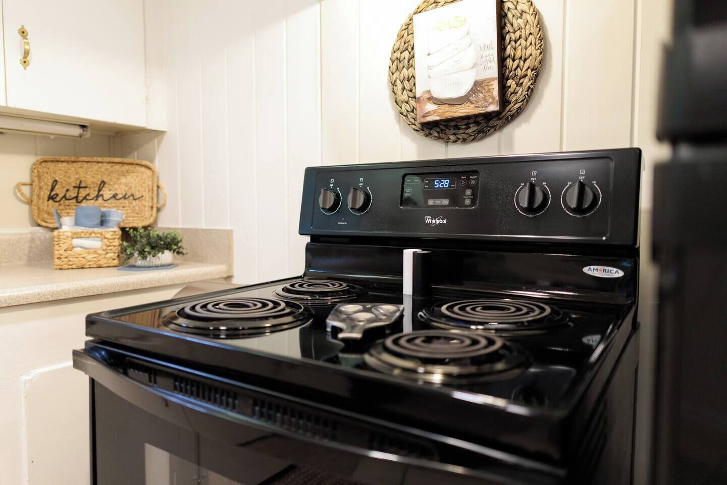 Una cocina con una estufa Whirlpool negra, cuatro hornillas y un panel de control digital.
