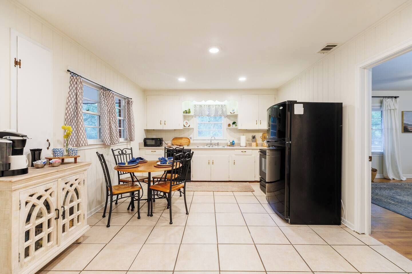A compact kitchen with white cabinetry, a dining table with chairs, a black refrigerator, and a microwave.