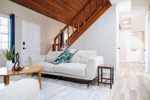 Ein Wohnzimmer mit einem weißen Sofa, einem Holztisch und einer Treppe mit hölzernen Geländern.