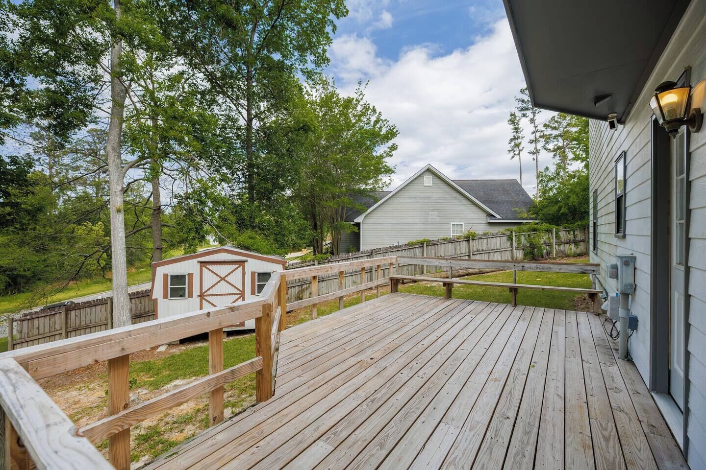 A wooden deck with a small shed and a house in the background.