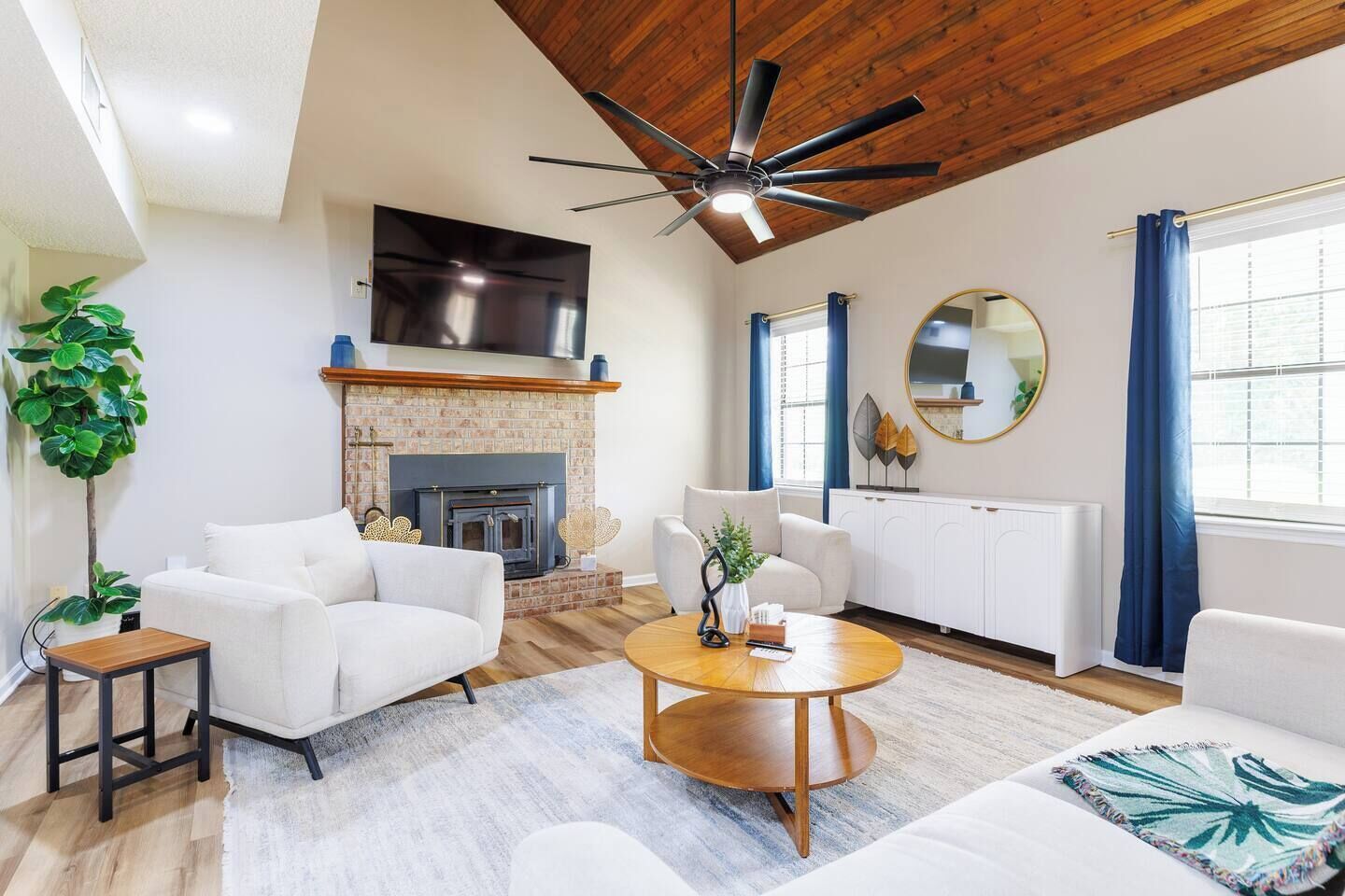 Una sala de estar moderna con chimenea, sofás blancos, una mesa de centro y un ventilador de techo.