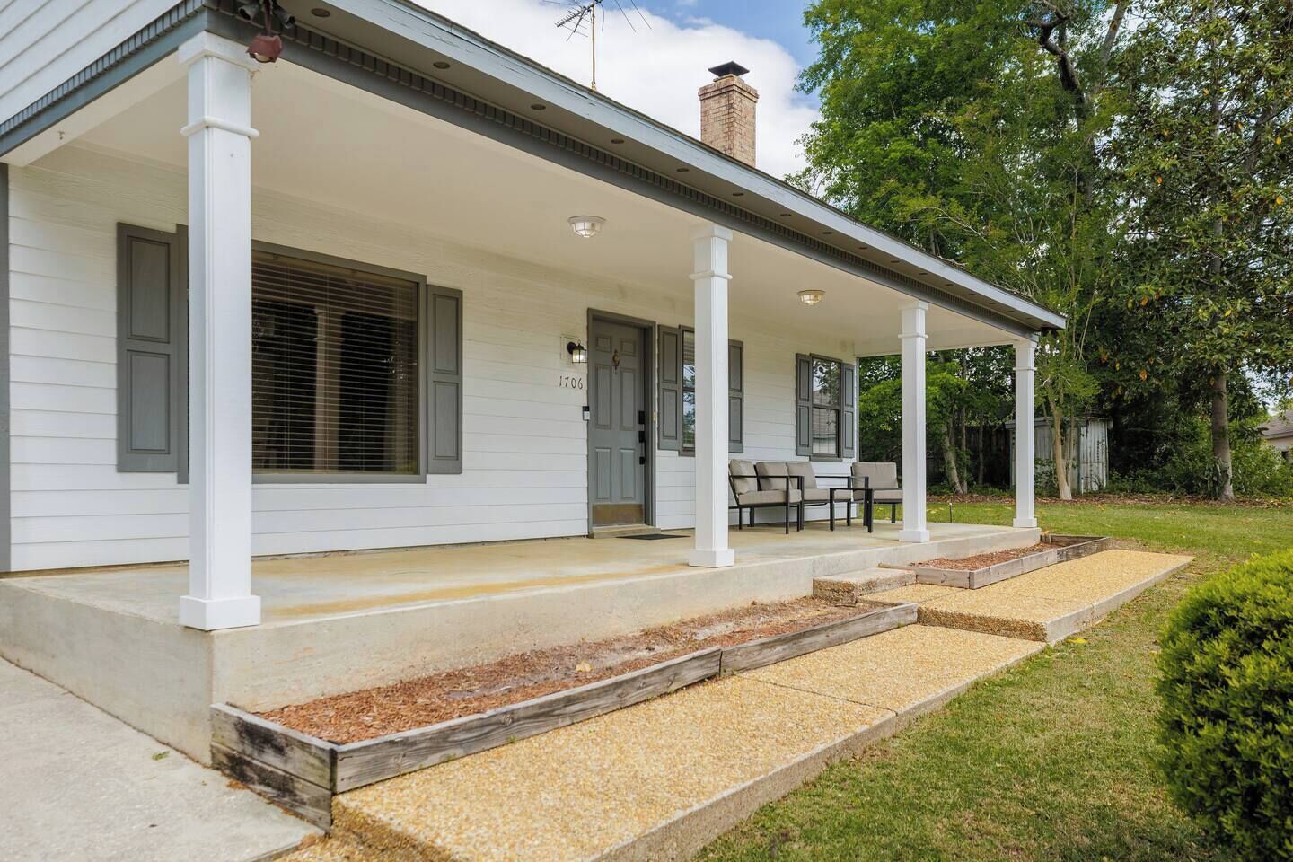 A white house with a covered porch, a chimney, and a number '1706' on the door.