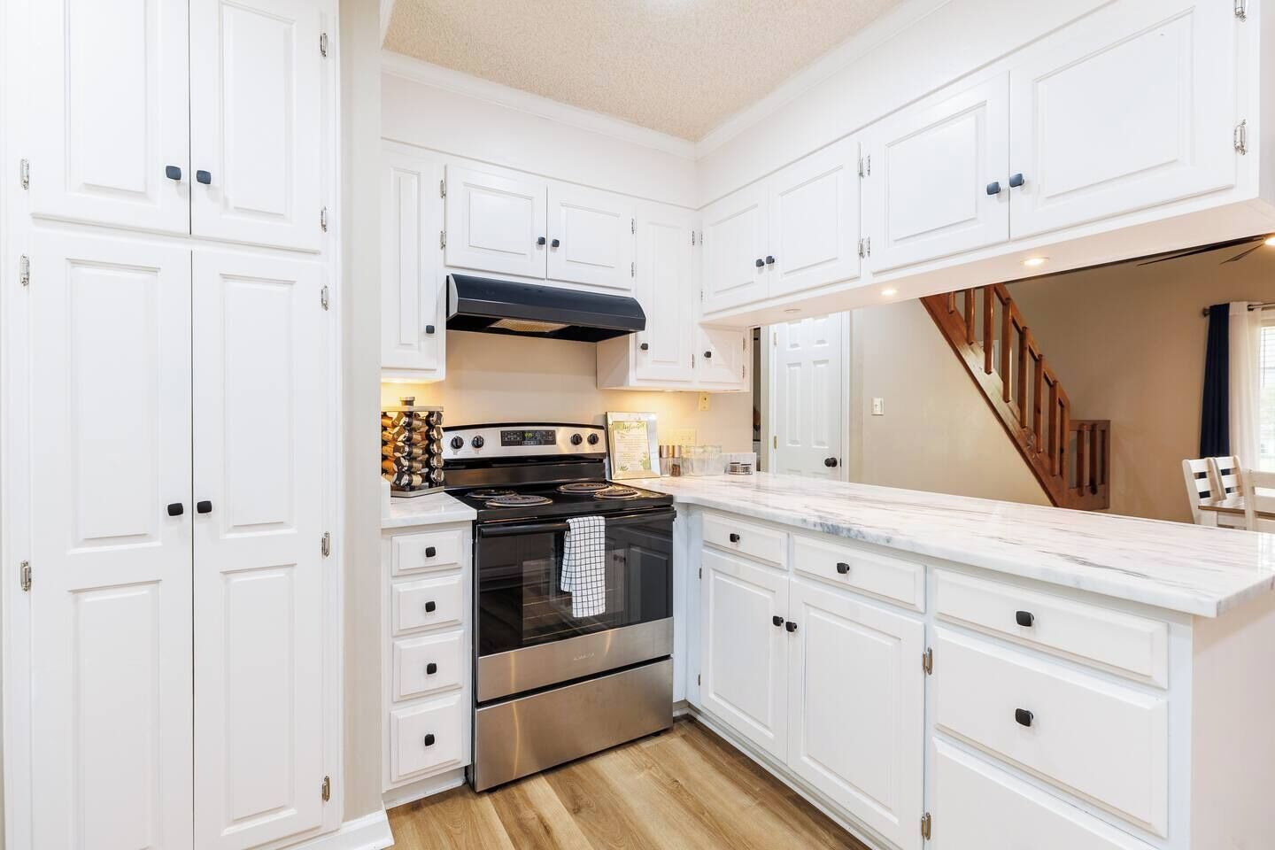 Una cocina con muebles blancos, estufa de acero inoxidable y una escalera de madera.