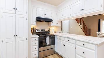 Una cocina con muebles blancos, estufa de acero inoxidable y una escalera de madera.