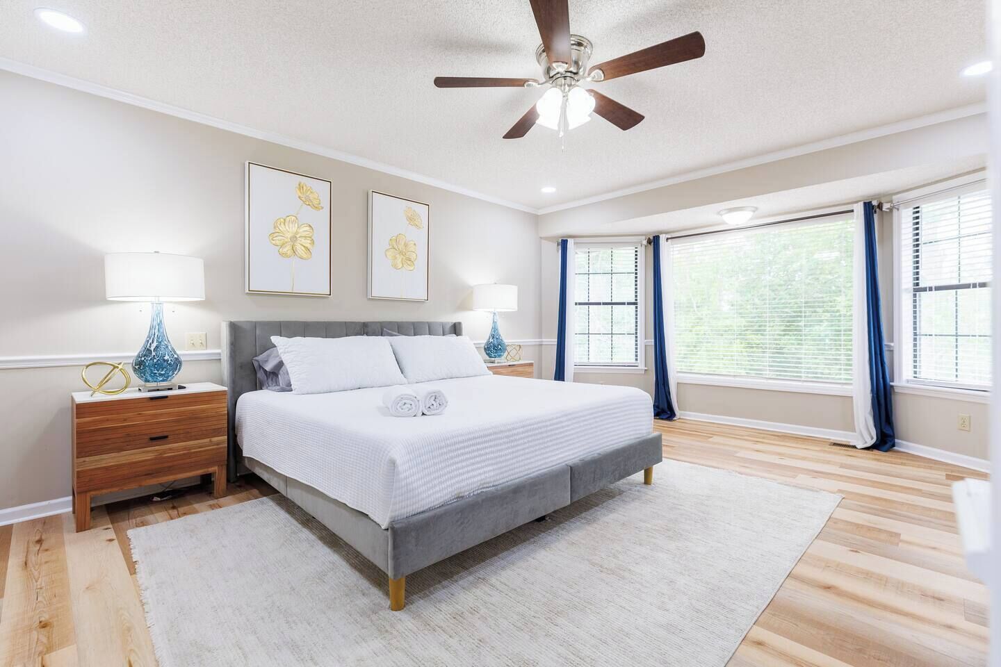 A bedroom with a bed, bedside tables, a ceiling fan, and large windows with curtains.