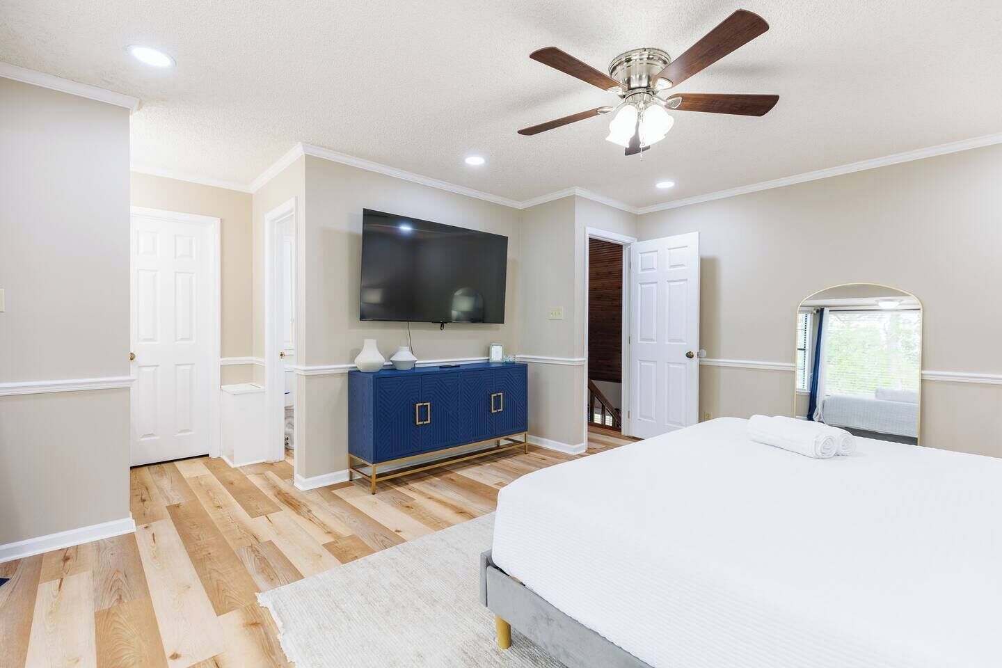Une chambre à coucher avec un lit, une commode bleue, un ventilateur de plafond et un téléviseur.