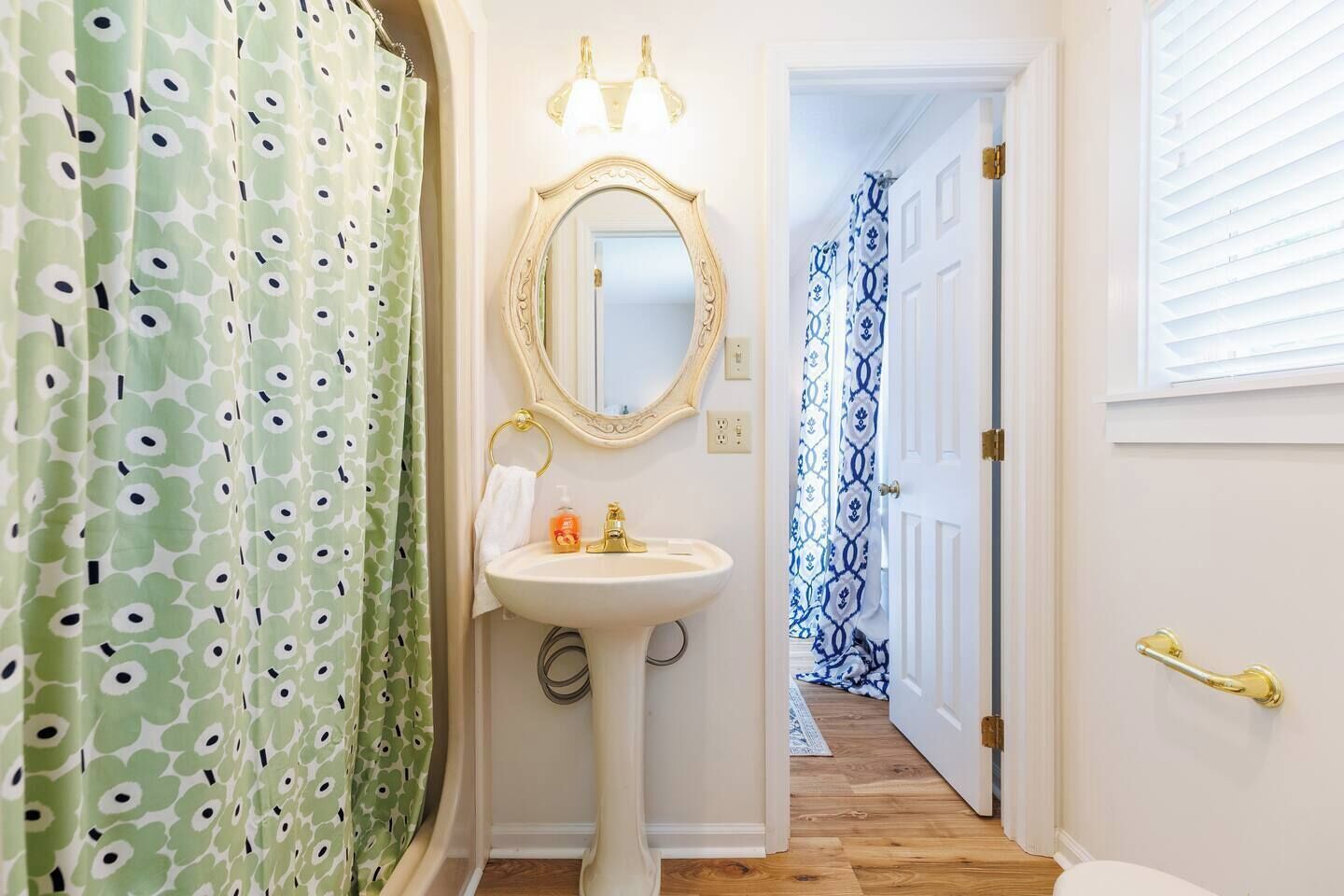 Une salle de bain avec un lavabo sur colonne, un miroir et un rideau de douche à motifs floraux.