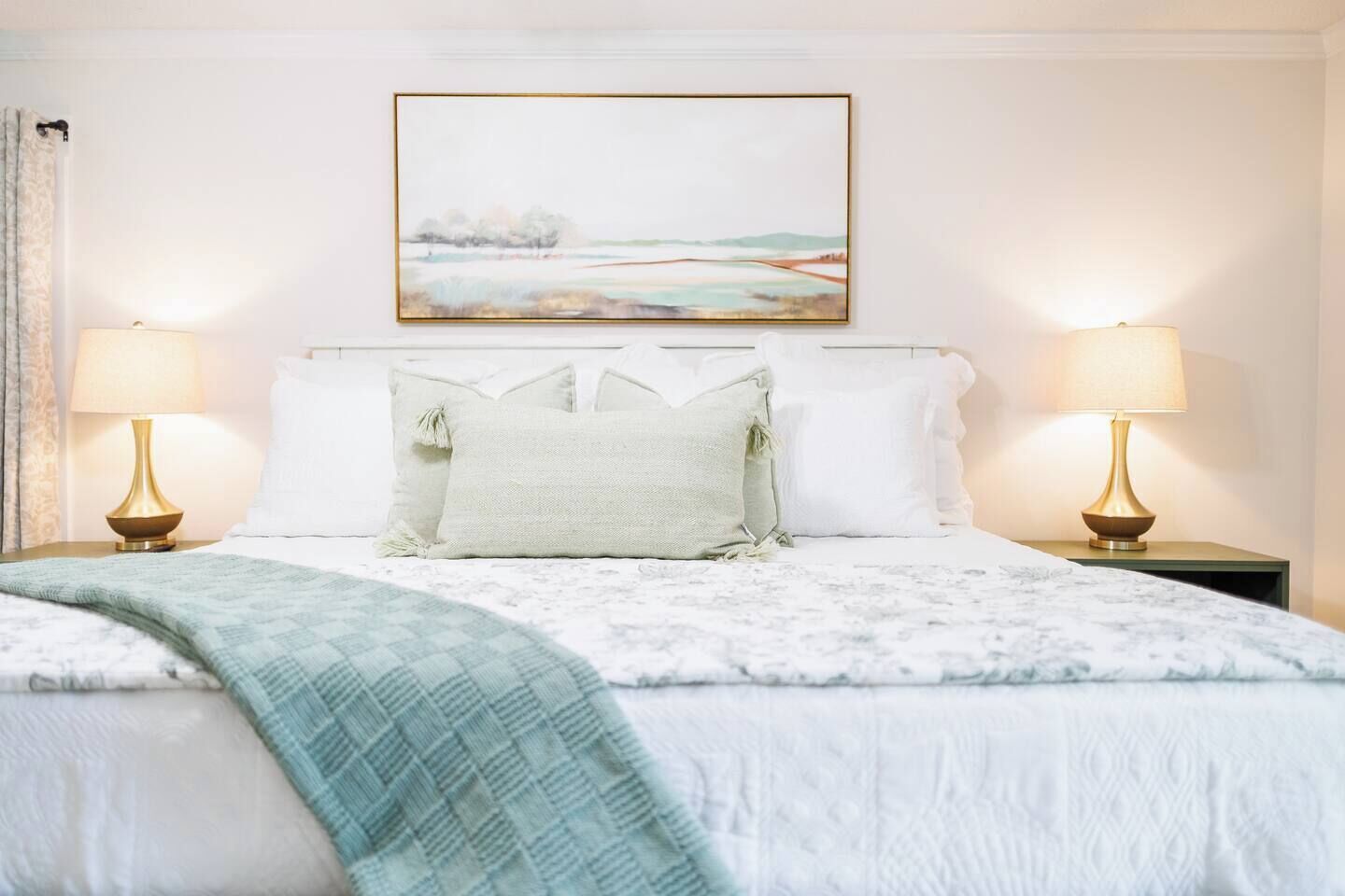Habitación de hotel con cama, dos lámparas de noche, un cuadro en la pared y una ventana con cortinas.