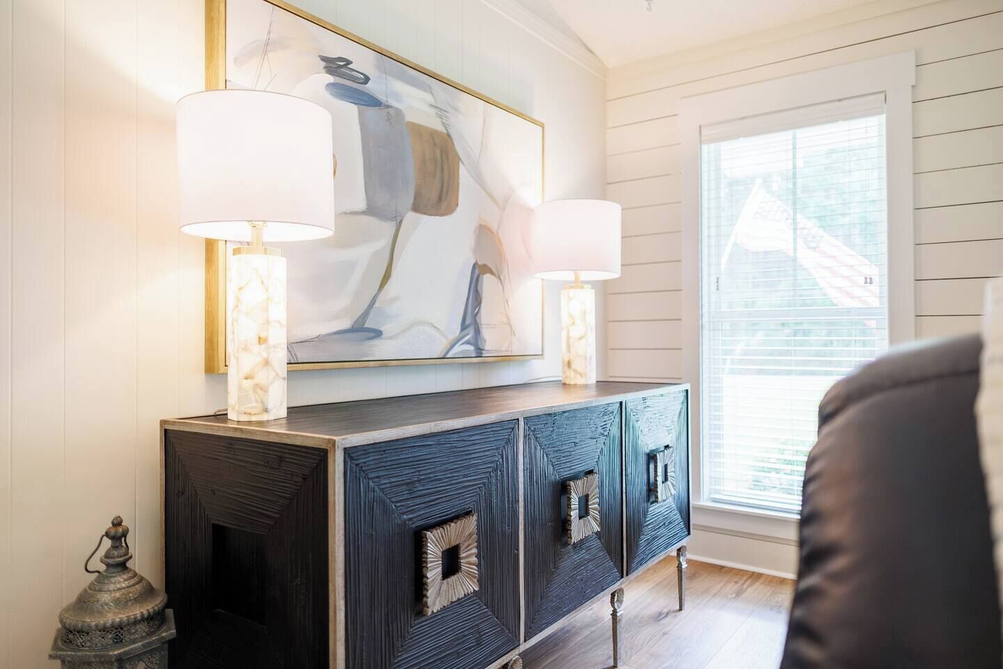 A room with a dark wood cabinet, two wall-mounted lamps, and a large abstract painting above the cabinet.
