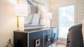 A room with a dark wood cabinet, two wall-mounted lamps, and a large abstract painting above the cabinet.