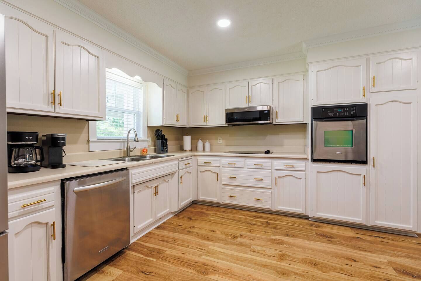 Una cocina con armarios blancos, electrodomésticos de acero inoxidable y piso de madera.