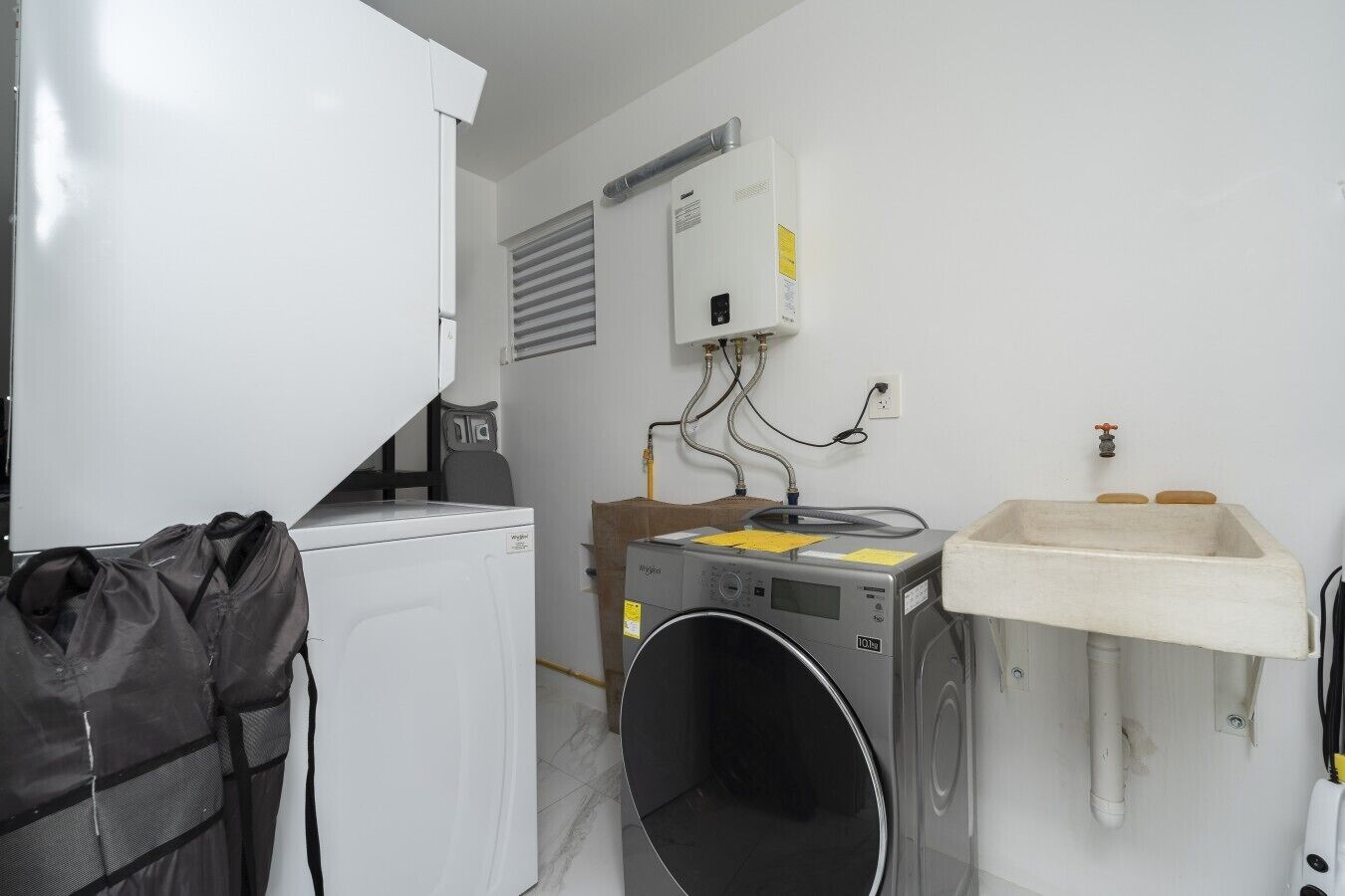A laundry room with a washing machine, a dryer, a sink, and a bag of clothes.
