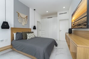 A modern bedroom with a bed, bedside lamps, a wall-mounted artwork, and a wardrobe. - Heart of Cabo|3BR Oasis|Rooftop Spa|Poolside (Cabo San Lucas)