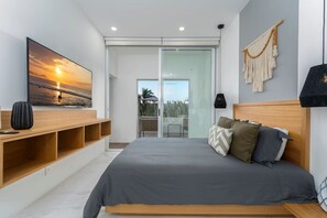A modern bedroom with a large bed, a TV mounted on the wall, and a sliding glass door leading to a balcony. - Heart of Cabo|3BR Oasis|Rooftop Spa|Poolside (Cabo San Lucas)