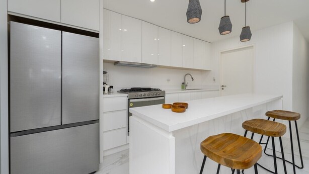 A modern kitchen with white cabinetry, a stainless steel refrigerator, a gas stove, and wooden stools. - Heart of Cabo|3BR Oasis|Rooftop Spa|Poolside (Cabo San Lucas)