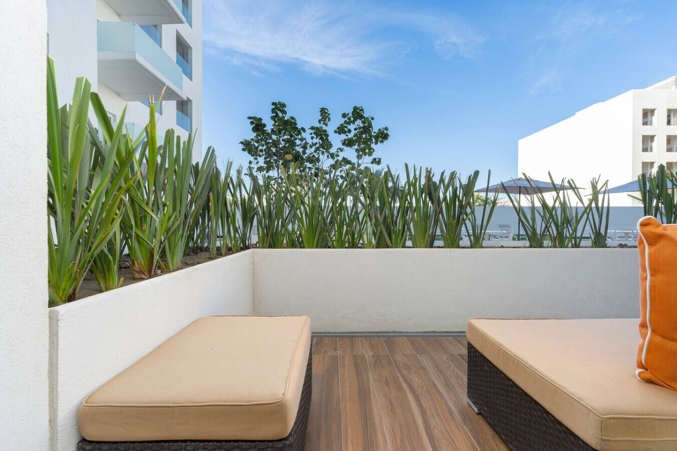 Een balkon met twee beige zithoeken, een houten vloer en uitzicht op gebouwen en groen.